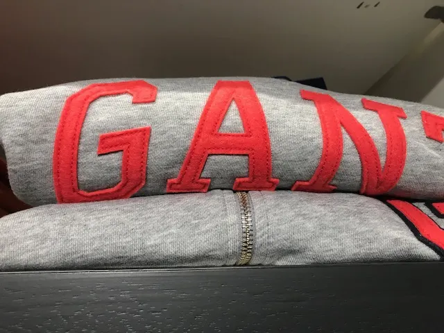 Grijze GANT-trui met rood logo, gevouwen op een plank